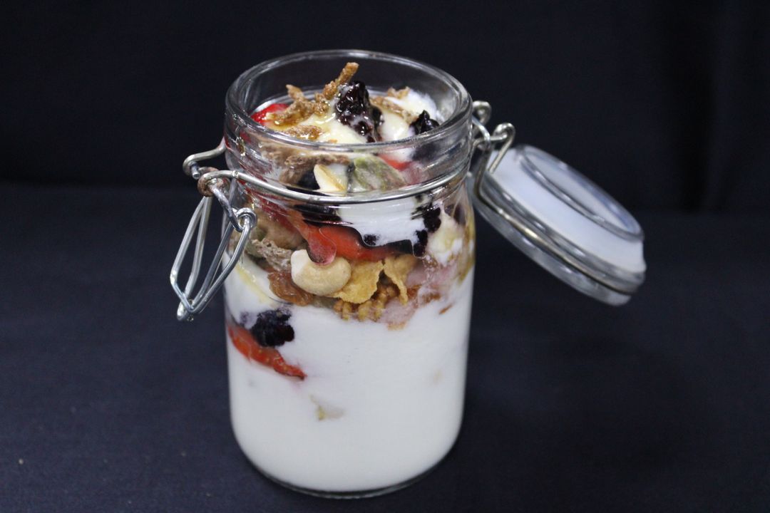 Plain yogurt mixed with granola, strawberries, blue berries topped with honey 